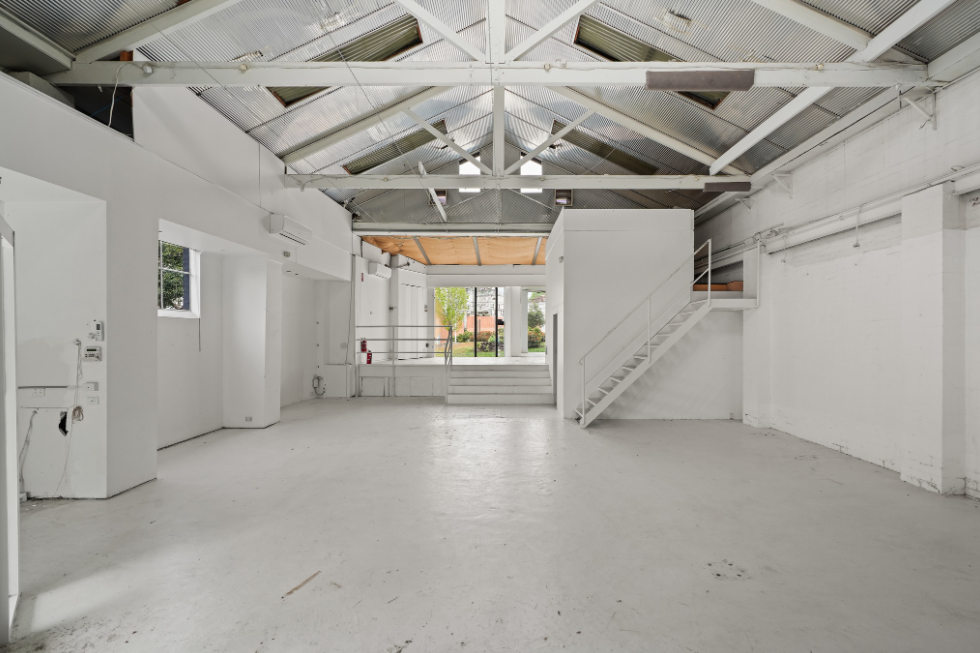 Spacious white industrial-style pop-up shop interior with exposed beams, high ceilings, concrete flooring, and a staircase leading to a mezzanine area